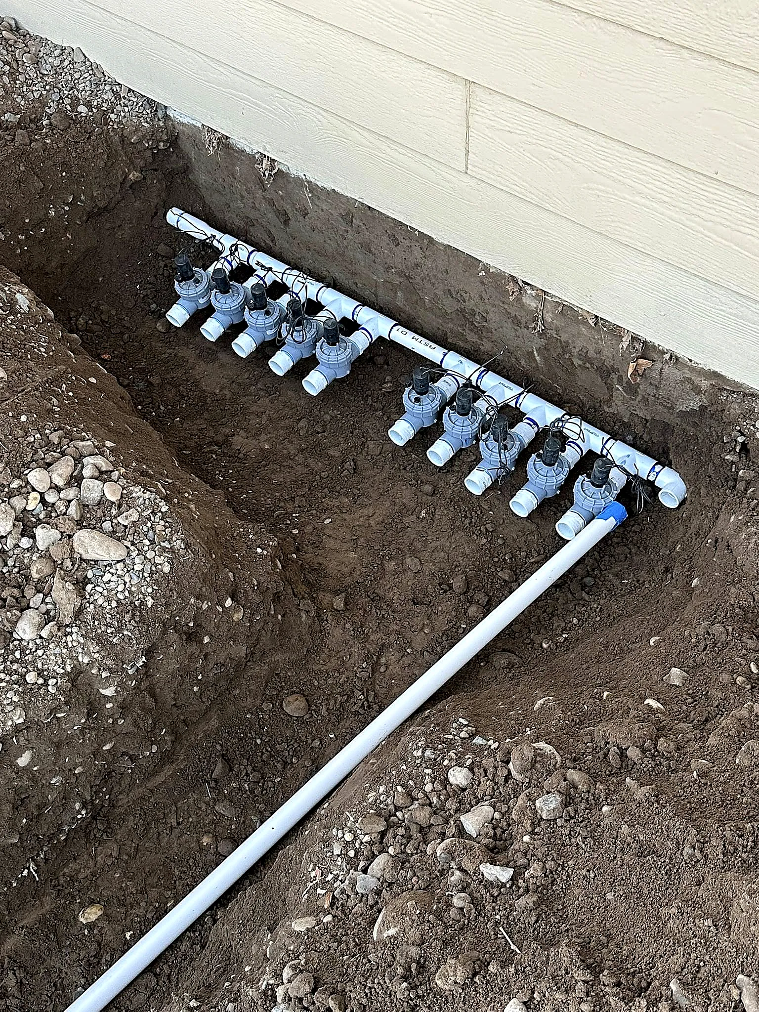 A new irrigation manifold with a bank of valves installed in a trench, ready to be programmed and buried